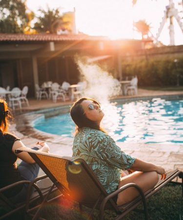 woman in white and black floral shirt sitting on chair near swimming pool during daytime