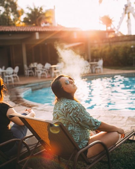 woman in white and black floral shirt sitting on chair near swimming pool during daytime