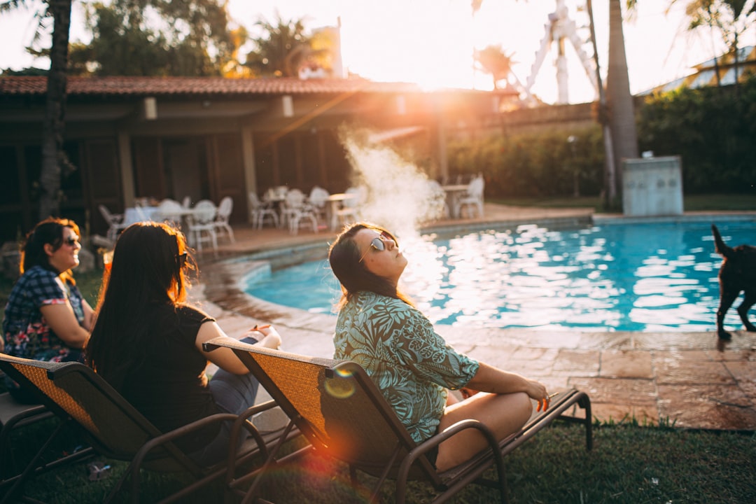 woman in white and black floral shirt sitting on chair near swimming pool during daytime