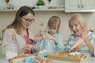 Three women baking and decorating cupcakes in a kitchen.