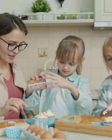 Three women baking and decorating cupcakes in a kitchen.