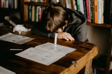 boy in gray hoodie reading book on brown wooden table