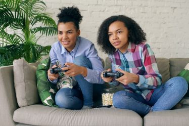 Two young women playing video games on a couch